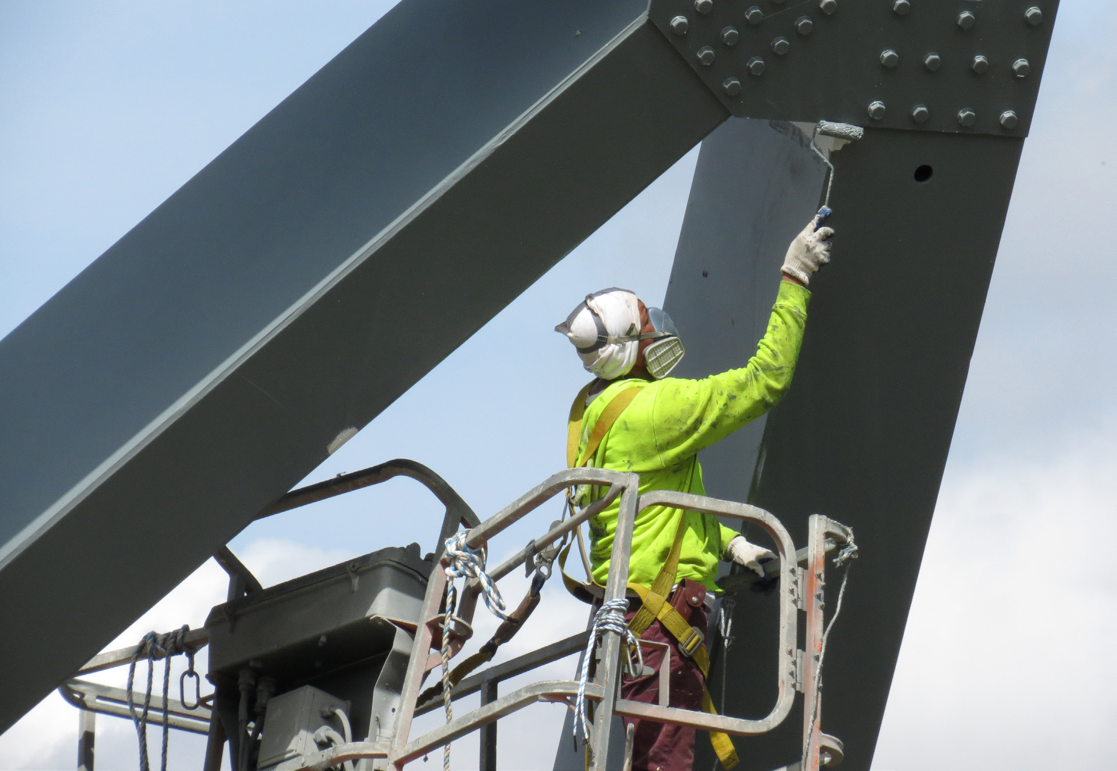 an image of a worker in a safety harness painting a bridge