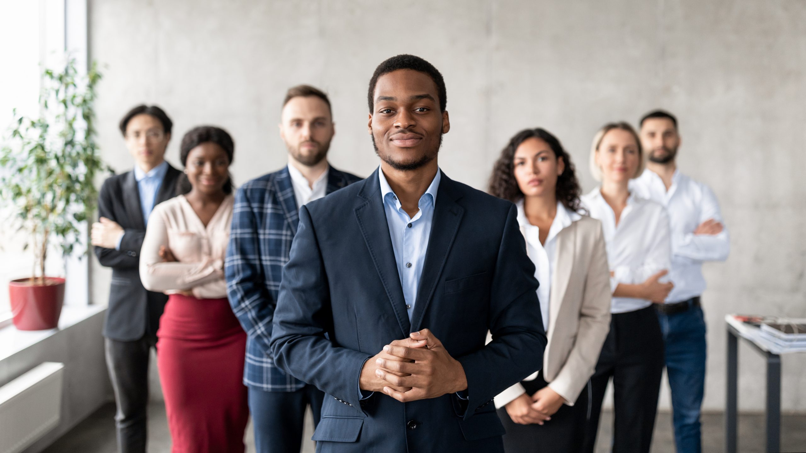 Leadership. Successful African Businessman Standing With His Business Team In Modern Office, Smiling To Camera. Career Growth Motivation, Entrepreneurship Concept. Selective Focus, Panorama